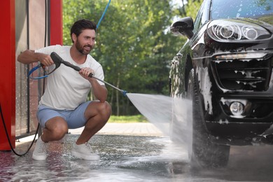 Photo of Happy man washing auto with high pressure water jet at outdoor car wash