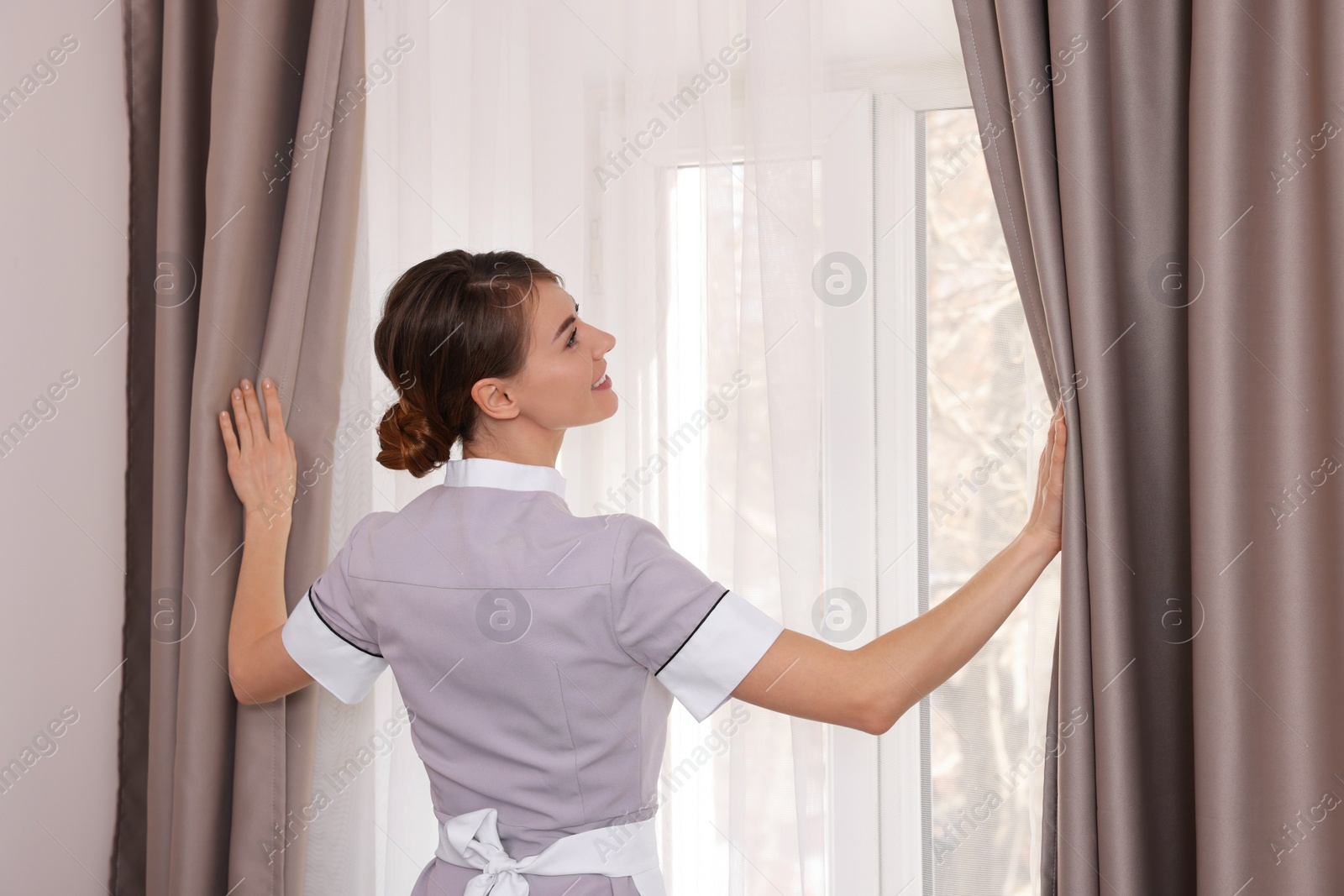 Photo of Beautiful chambermaid opening window curtains in hotel room