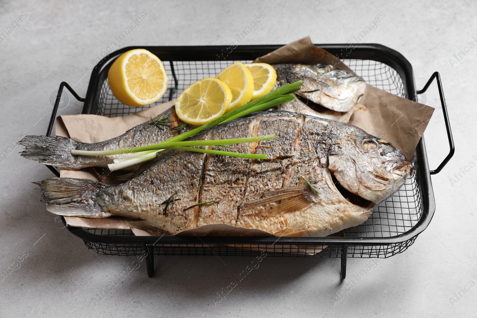 Photo of Seafood. Delicious baked fish served with green onion and lemon on light textured table, closeup