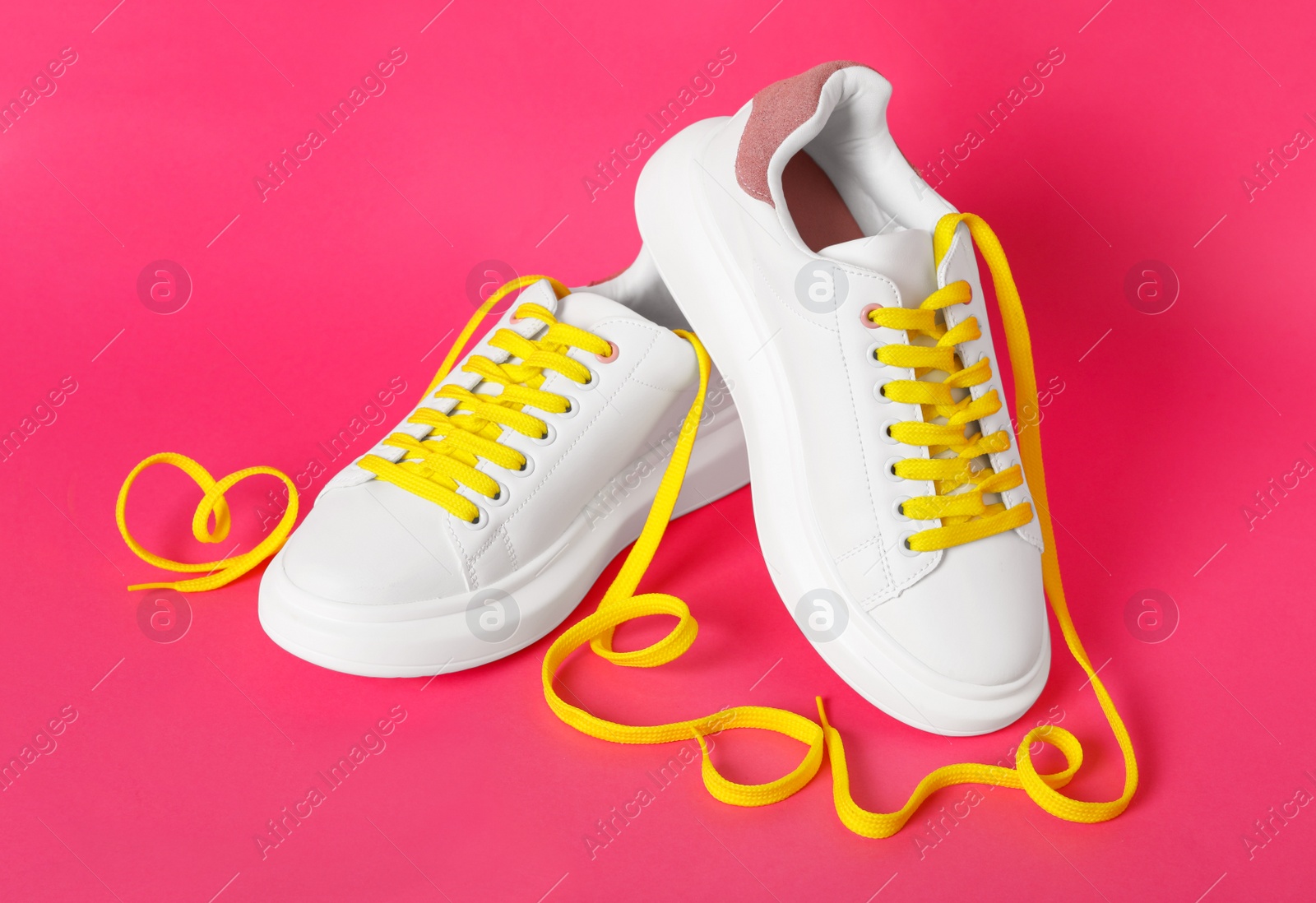 Photo of Pair of stylish shoes with yellow laces on pink background