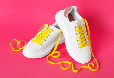 Pair of stylish shoes with yellow laces on pink background