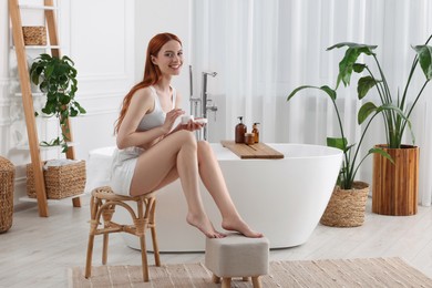 Photo of Beautiful young woman with body cream in bathroom, space for text
