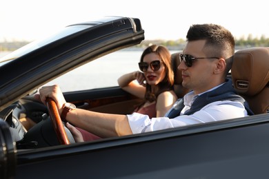 Stylish couple driving luxury convertible car outdoors