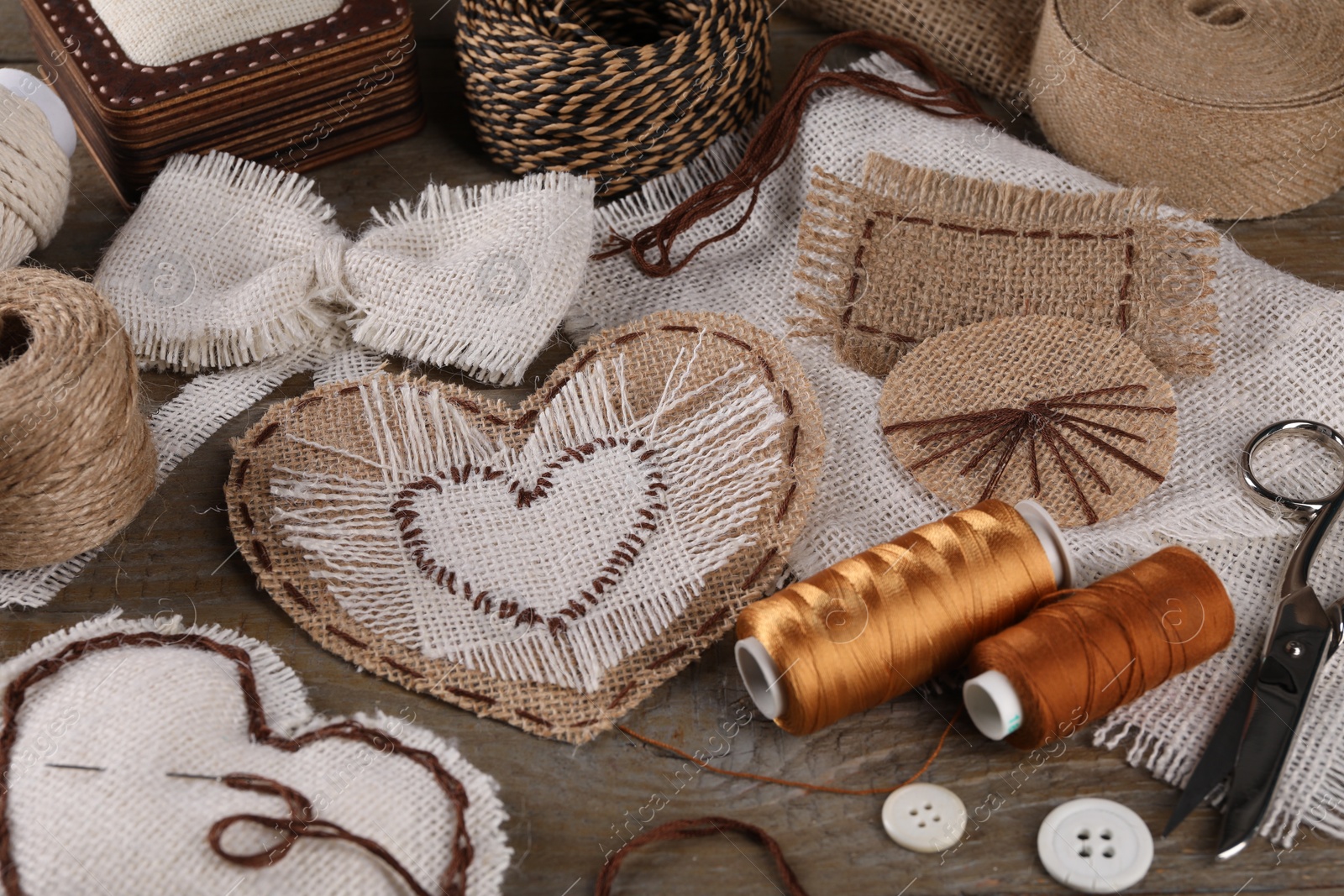 Photo of Pieces of burlap fabric with different stitches and sewing tools on wooden table, closeup