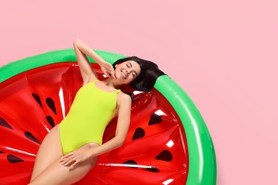 Photo of Young woman wearing stylish swimsuit on inflatable mattress against pink background