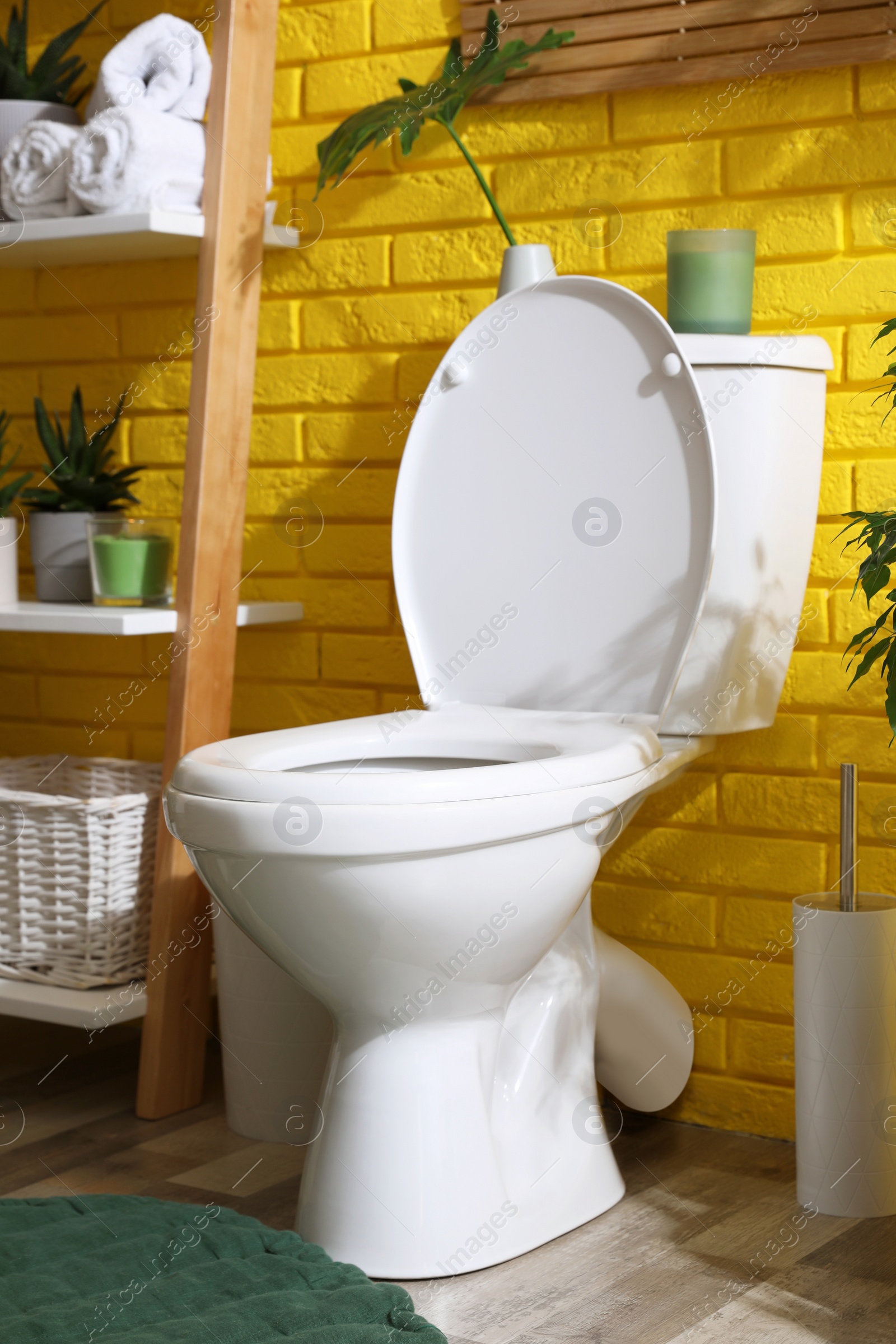 Photo of Stylish bathroom with toilet bowl and green plants near yellow brick wall. Interior design