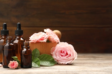 Photo of Bottles of rose essential oil and flowers on wooden table, space for text