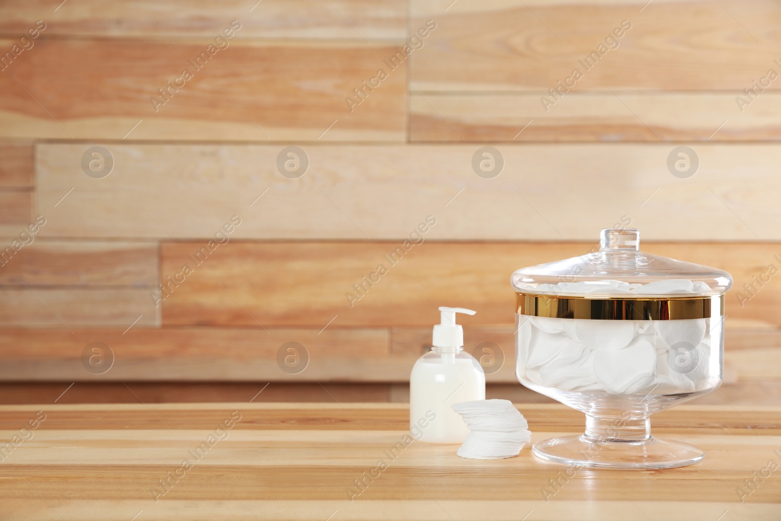 Photo of Decorative glass jar with cotton pads and cosmetic product on table against wooden background. Space for text