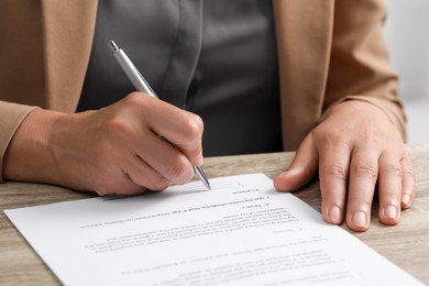 Photo of Woman signing document at wooden table indoors, closeup