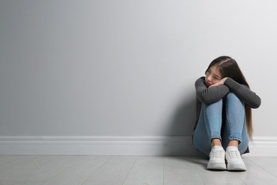 Photo of Upset teenage girl sitting on floor near wall. Space for text