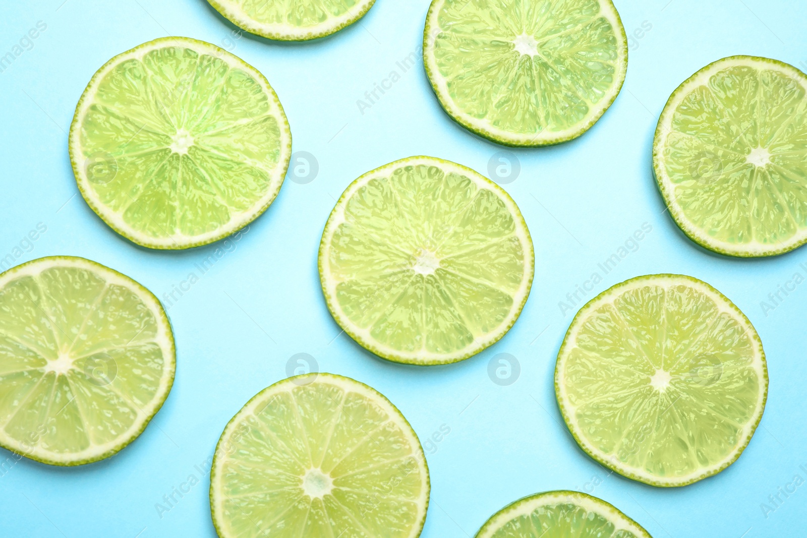 Photo of Fresh juicy lime slices on light blue background, flat lay