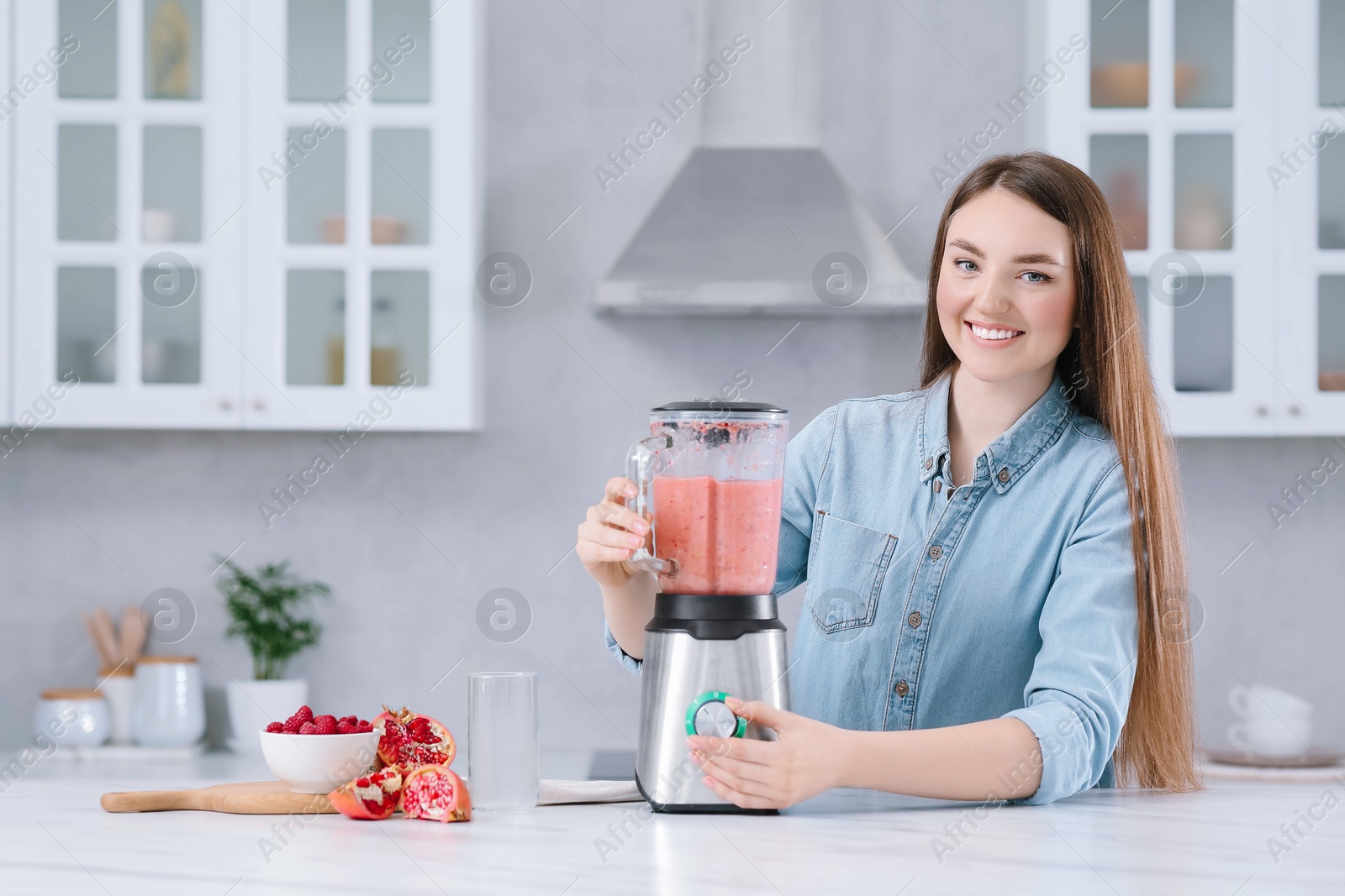 Photo of Beautiful young woman preparing tasty smoothie at white table in kitchen. Space for text