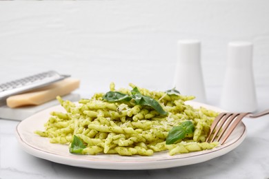 Plate of delicious trofie pasta with pesto sauce, cheese and basil leaves on white marble table