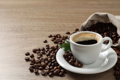 Photo of Cup of aromatic hot coffee and beans on wooden table. Space for text
