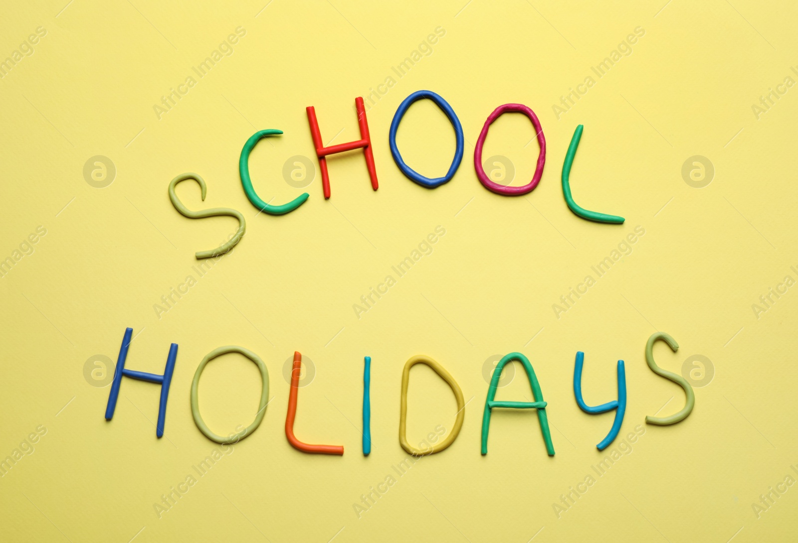 Photo of Text School Holidays made of modelling clay on yellow background, flat lay