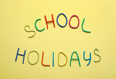 Text School Holidays made of modelling clay on yellow background, flat lay