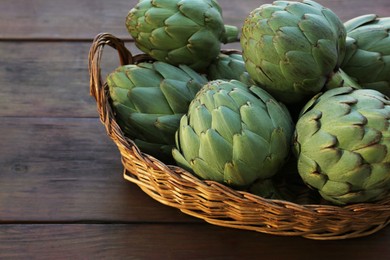 Photo of Wicker basket with fresh raw artichokes on wooden table, closeup