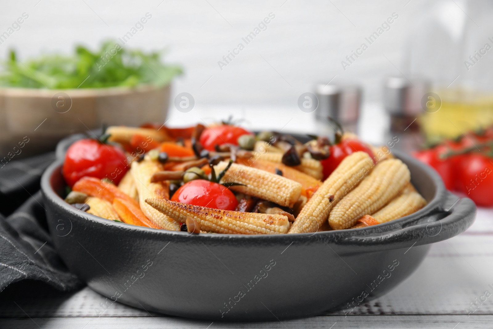 Photo of Tasty roasted baby corn with tomatoes, capers and mushrooms on white wooden table, closeup