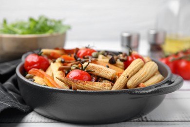 Tasty roasted baby corn with tomatoes, capers and mushrooms on white wooden table, closeup