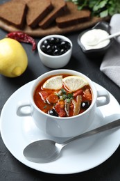 Meat solyanka soup with sausages, olives and vegetables served on dark grey table