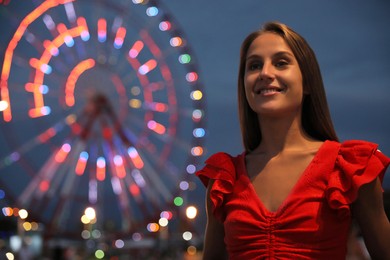 Beautiful young woman against glowing Ferris wheel in amusement park, space for text