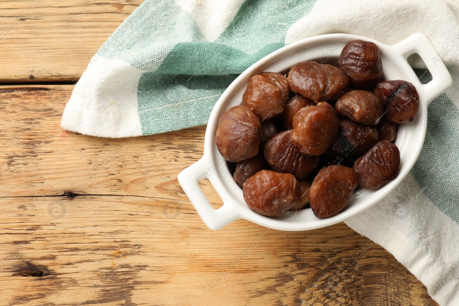 Photo of Roasted edible sweet chestnuts in dish on light wooden table, top view. Space for text