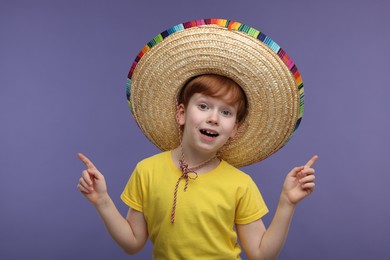 Photo of Surprised boy in Mexican sombrero hat pointing at something on violet background