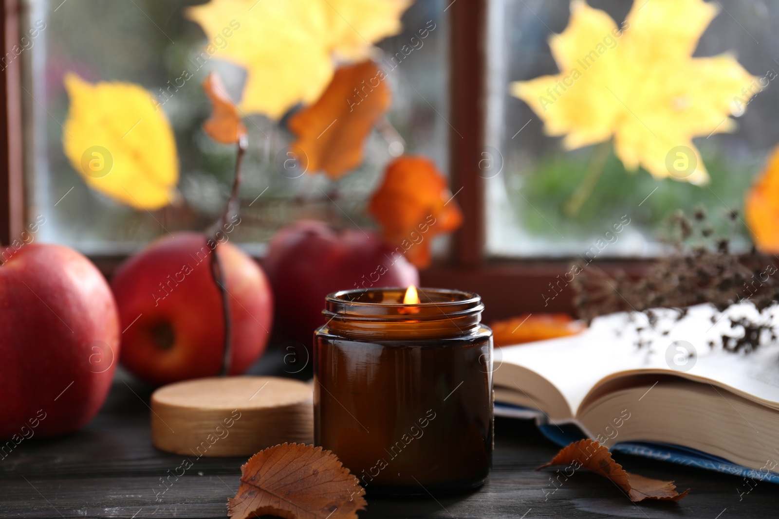 Photo of Beautiful burning candle and book on wooden table near window. Autumn atmosphere