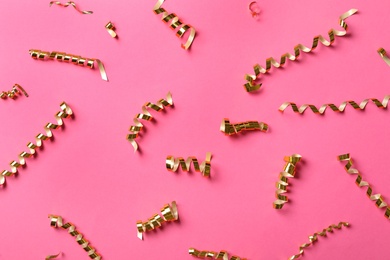 Photo of Shiny golden serpentine streamers on pink background, flat lay