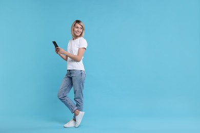 Happy woman with phone on light blue background, space for text