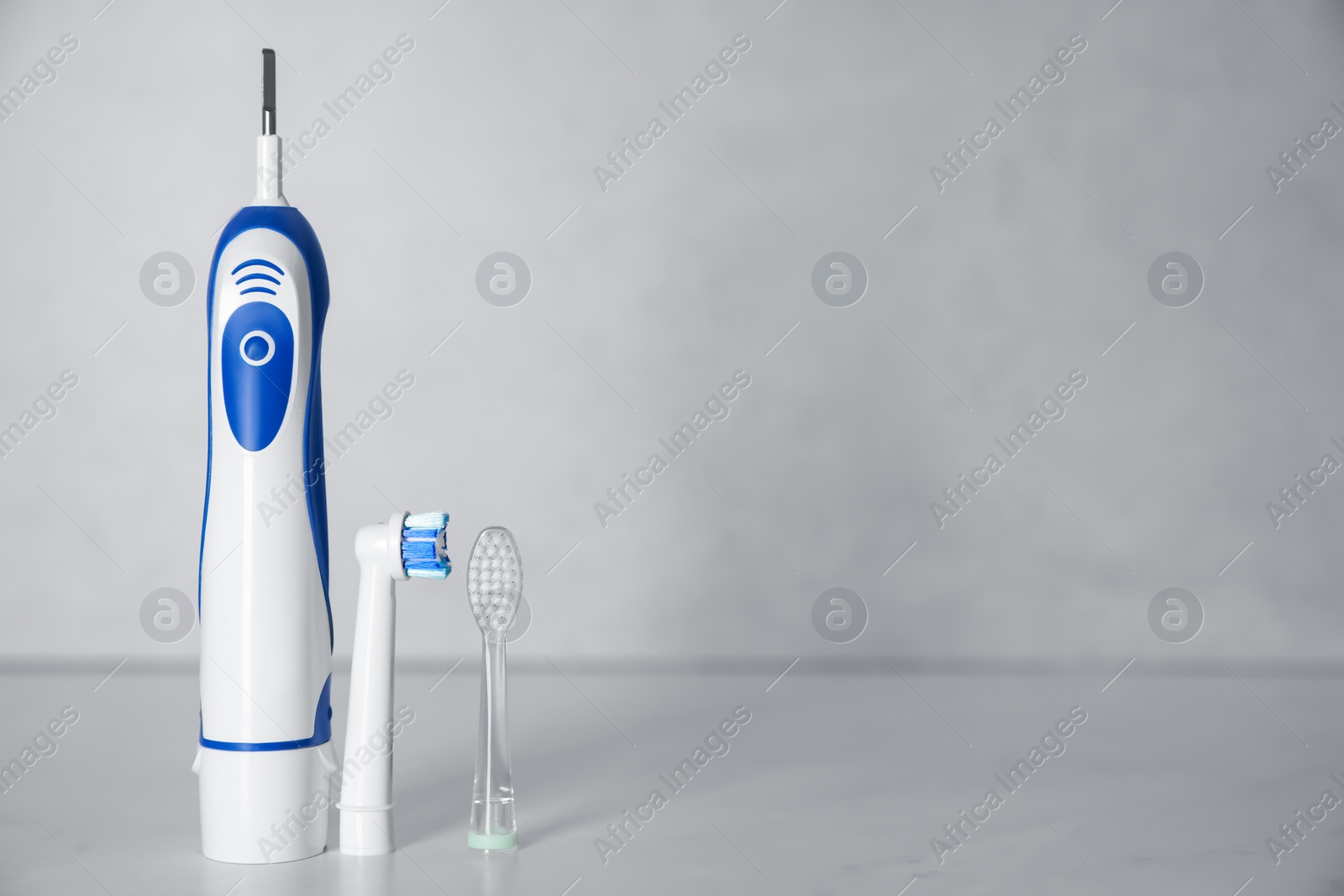 Photo of Electric toothbrush and replacement brush heads on light background, space for text