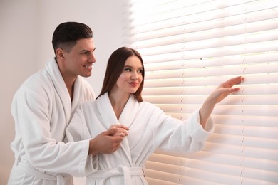 Photo of Happy couple wearing bathrobes near window at home