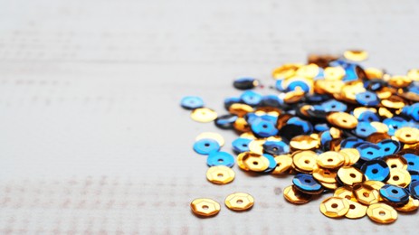 Photo of Pile of many yellow and blue sequins on white wooden table, closeup. Space for text