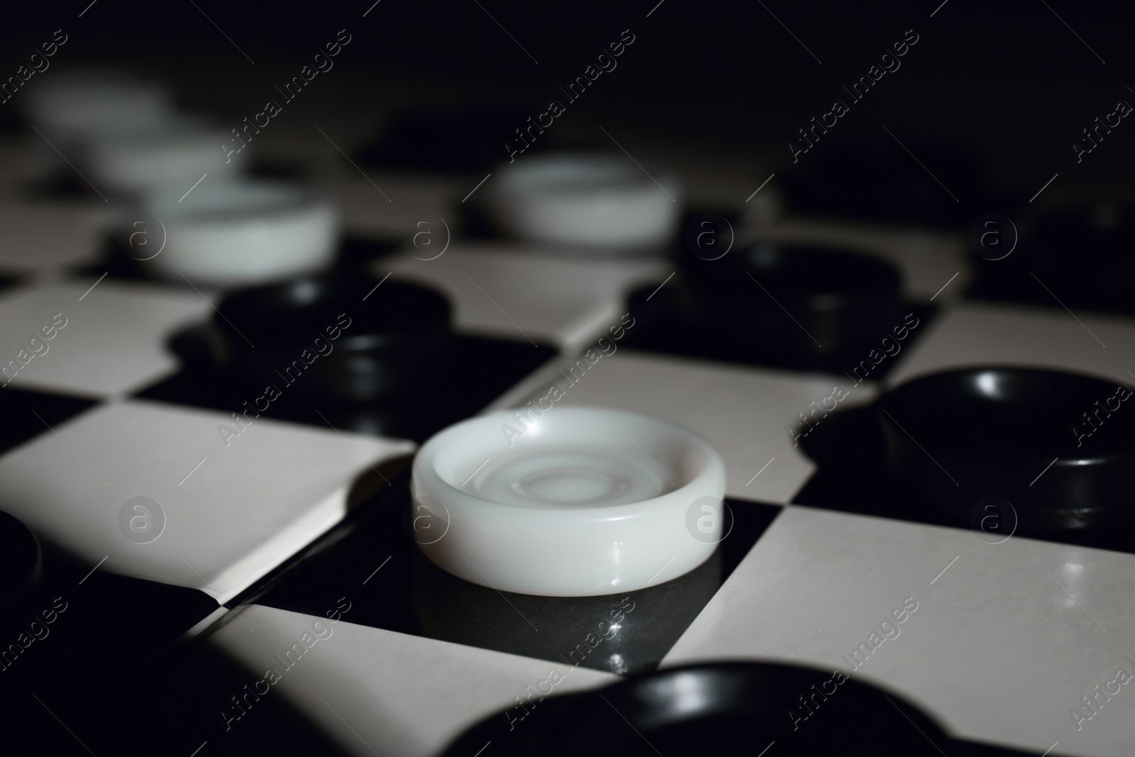 Photo of Checkerboard with game pieces on dark background, closeup