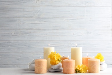 Photo of Composition of burning candles, spa stones and flowers on table. Space for text