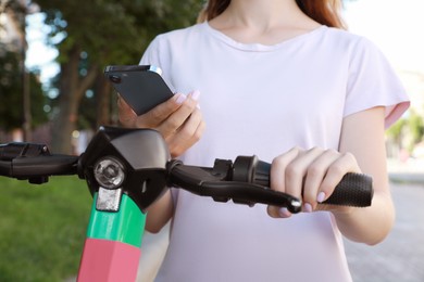 Photo of Woman using smartphone to pay and unblock electric kick scooter outdoors, closeup