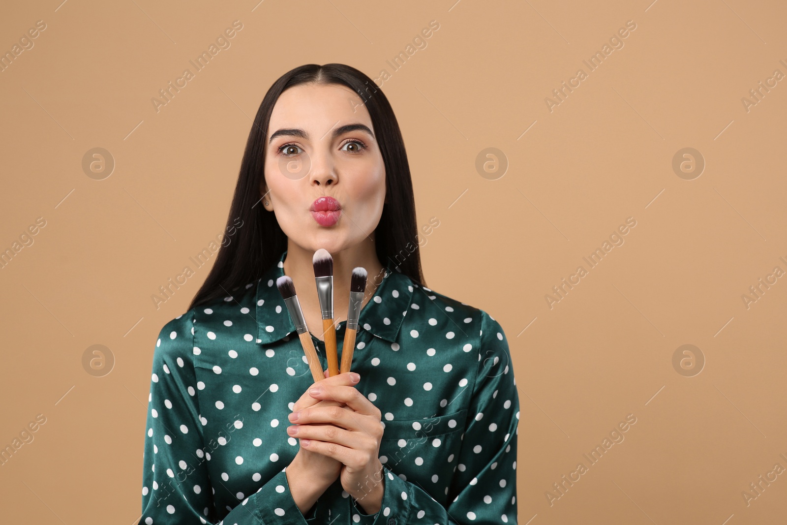 Photo of Beautiful woman with different makeup brushes on light brown background. Space for text