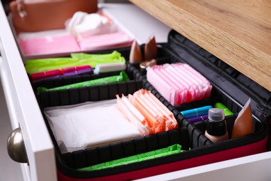 Photo of Open cabinet drawer with menstrual pads, tampons and skin care products, closeup
