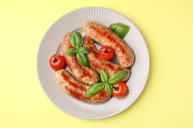 Photo of Plate with tasty homemade sausages, basil leaves and tomatoes on yellow table, top view