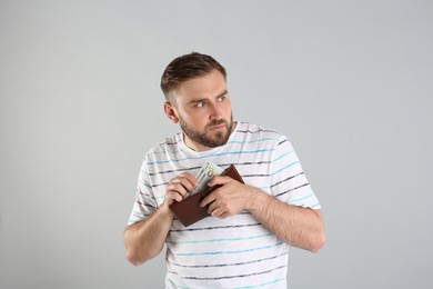 Greedy young man hiding wallet with money on light grey background