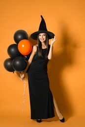 Beautiful woman wearing witch costume with balloons for Halloween party on yellow background