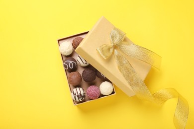 Photo of Open box with delicious chocolate candies on yellow background, top view