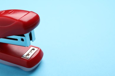 Photo of One red stapler on light blue background, closeup. Space for text