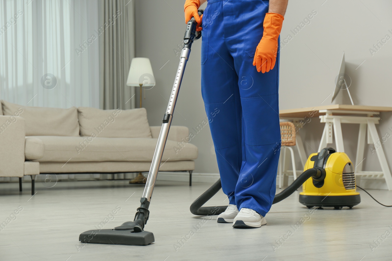 Photo of Janitor in uniform vacuuming floor indoors, closeup