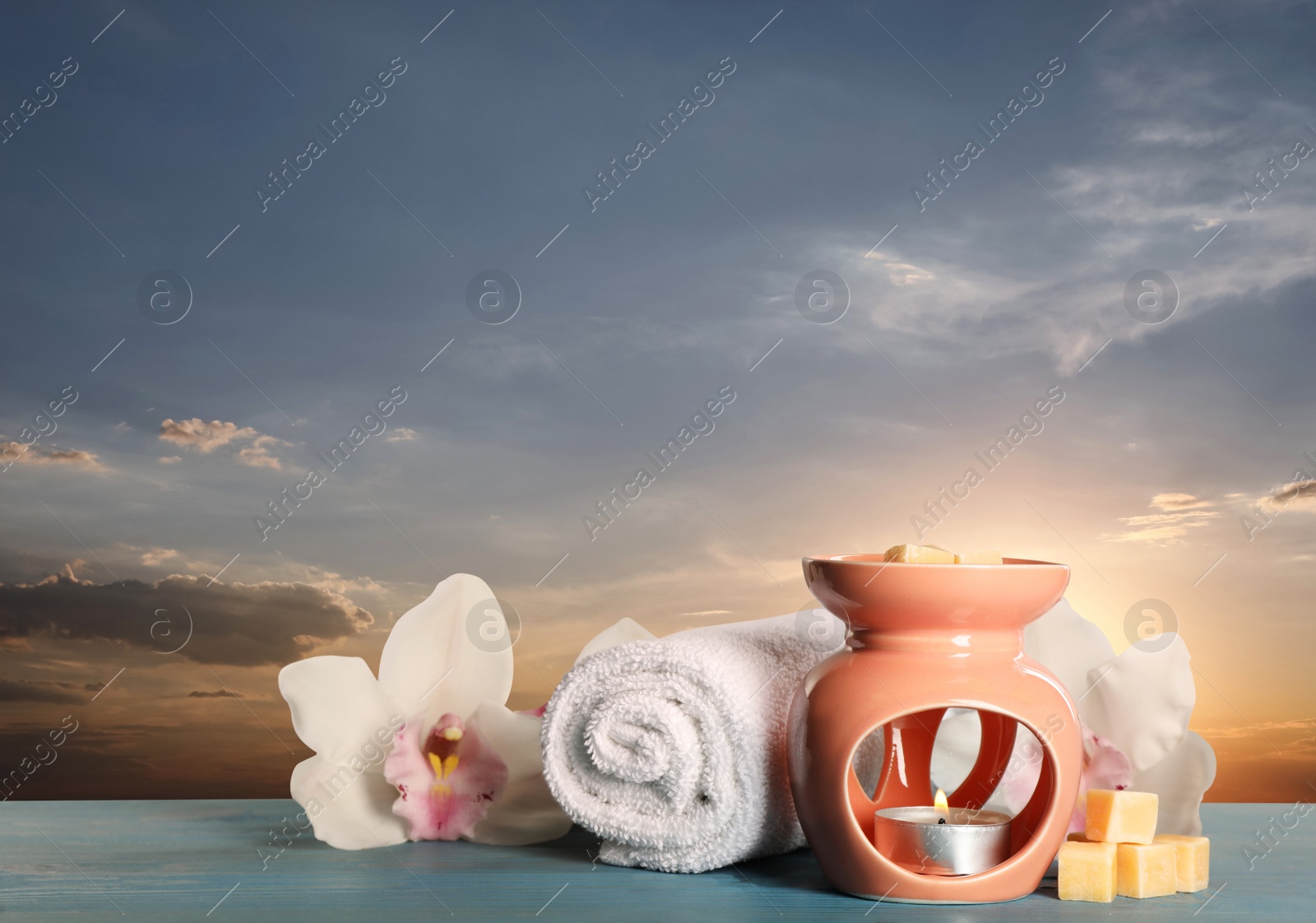 Image of Composition with aroma lamp on blue wooden table outdoors at sunset