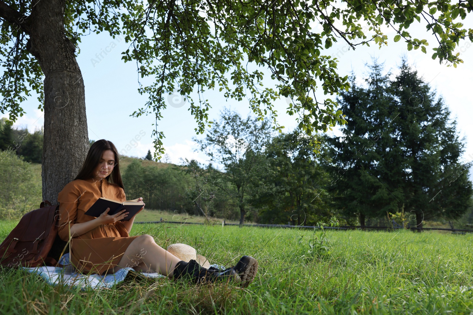 Photo of Young woman reading book under tree on meadow