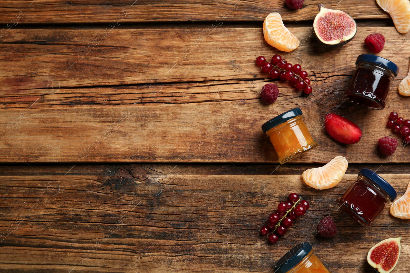 Photo of Jars of different jams and fresh ingredients on wooden table, flat lay. Space for text