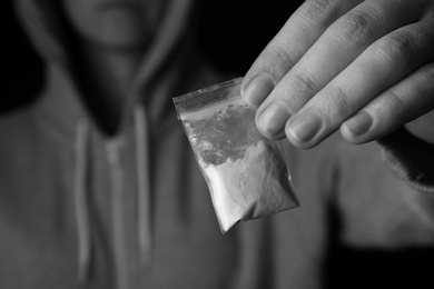 Drug dealer holding bag with cocaine on black background, closeup