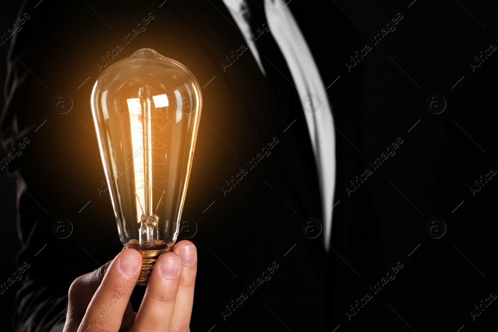 Photo of Businessman holding lamp bulb against dark background, closeup. Space for text