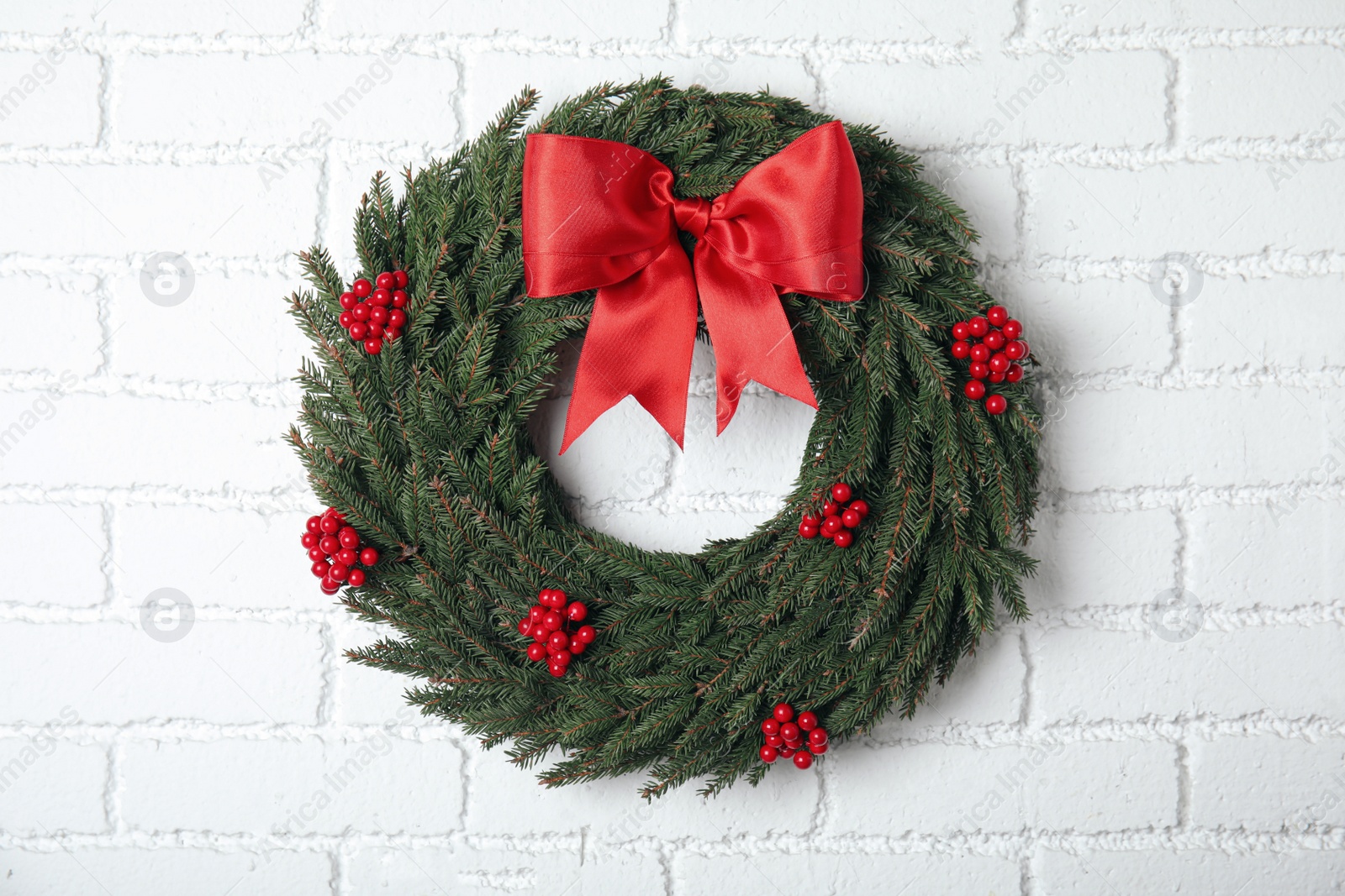 Photo of Beautiful Christmas wreath with red berries and bow hanging white brick wall